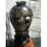 A BLACK LACQUERED AND POLYCHROME PEDESTAL of cylindrical form surmounted with an urn shaped vase