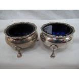 Pair of Georgian style circular silver salts with reeded border on three hoof feet (blue glass