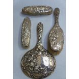 Four piece Art Nouveau chased silver back dressing table set - three brushes and a hand mirror