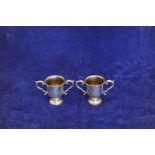 A pair of Elizabeth II silver twin handled cups with acanthus leaf capped scrolled handles, on