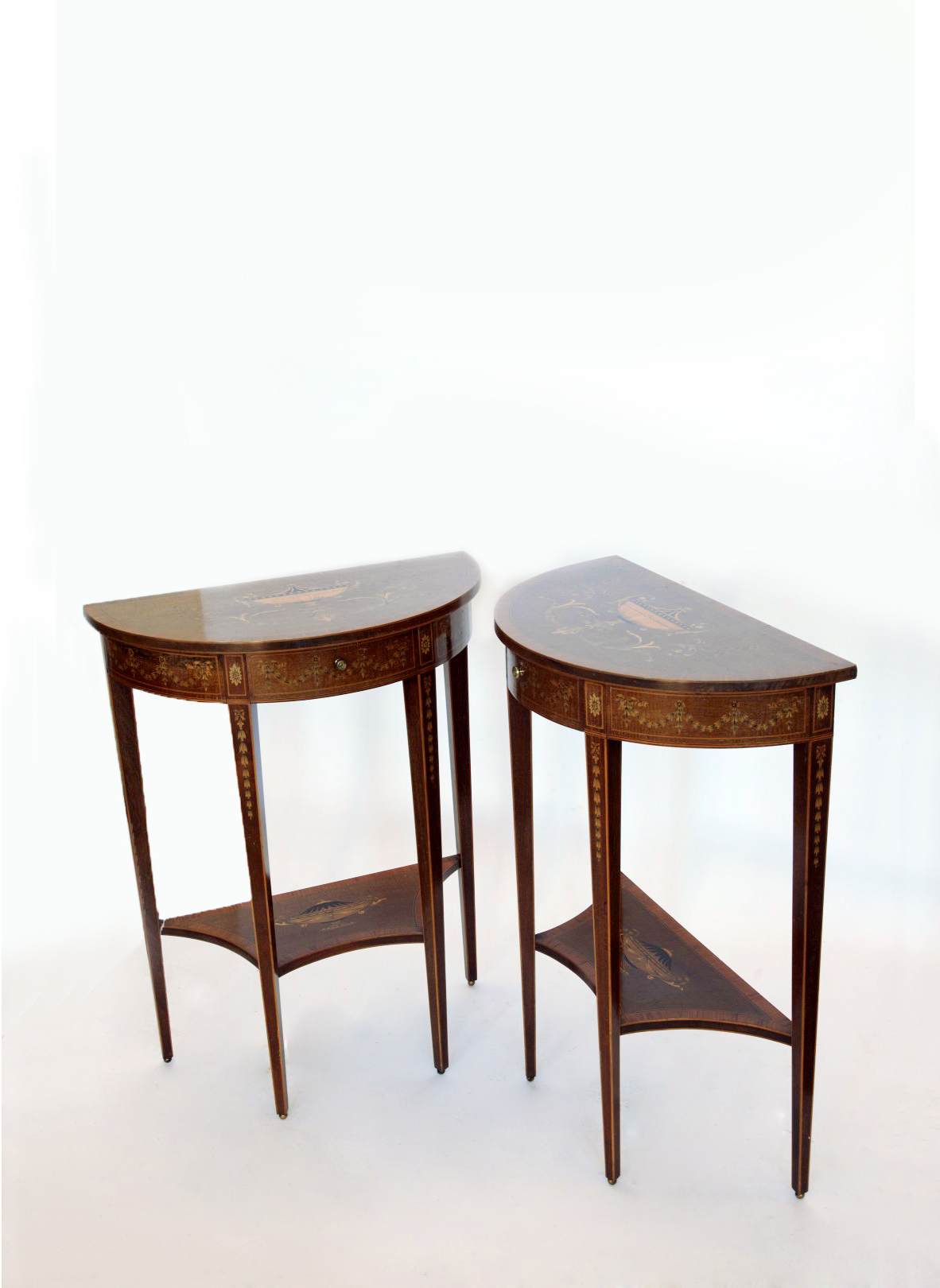 A pair of Edwardian demi-lune hall tables, the tops inlaid with a twin handled vase surrounded by