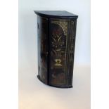A Chinoiserie style black lacquer decorated bow front hanging corner cupboard, the doors decorated