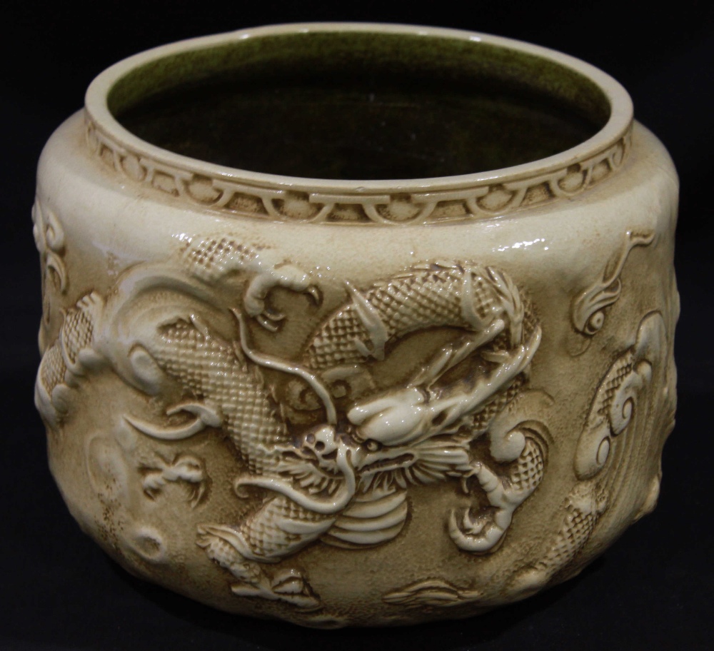 A Bretby pottery jardinière moulded with a continual dragon design to an 'antique' ivory ground,