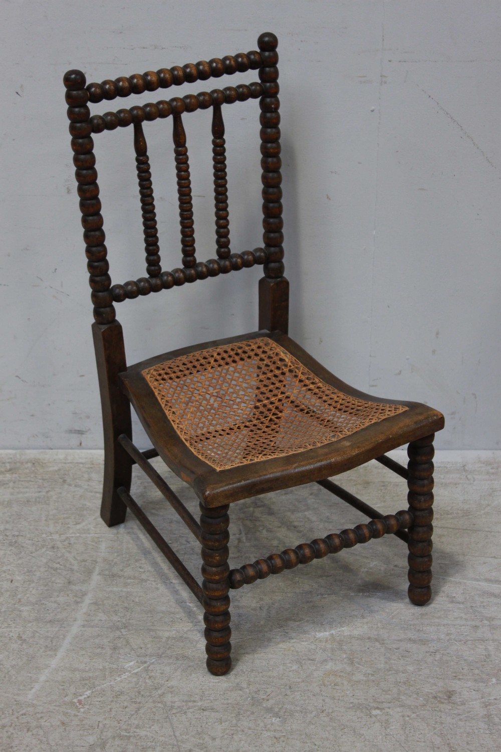 A stained beech wood bobbin turned chair, with rattan caned curved seat.