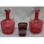 A pair of cranberry glass wine carafes and a ruby flash glass tumbler engraved with a view of Prague