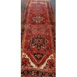 A hand-knotted long woollen Caucasian runner, red ground with five stylized eight-point floral