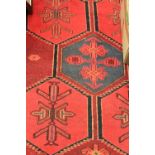 A hand-knotted woollen Caucasian carpet, deep red ground with a field of eleven hexagonal guls