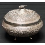 An Indian white metal embossed bowl and cover, surmounted with a bird, elaborately decorated with