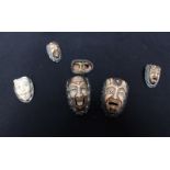 A collection of six Japanese carved bone and ivory mask brooches and rings, set in white metal.