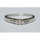 An 18ct white gold bar set solitaire diamond ring with three small diamonds channel set to each