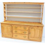 A large pine kitchen dresser with shaped cornice above three long open back shelves and hooks, the