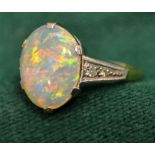An oval claw set cabochon opal ring having two small eight cut diamonds, on both shoulders, white