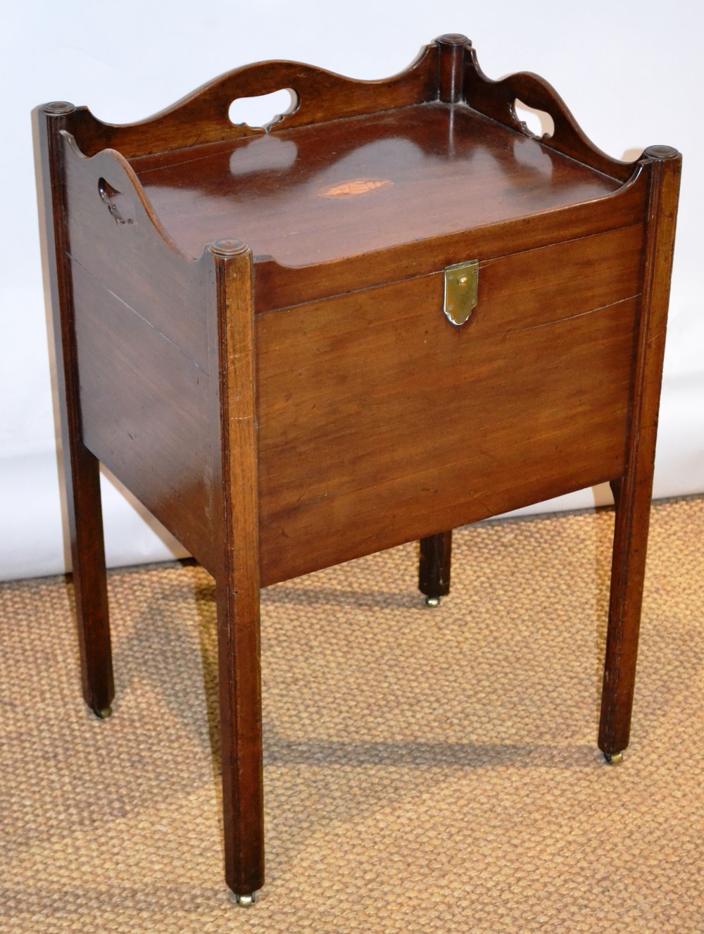 A Sheraton mahogany bedside cupboard, the serpentine shaped gallery top with pierced hand grips, a