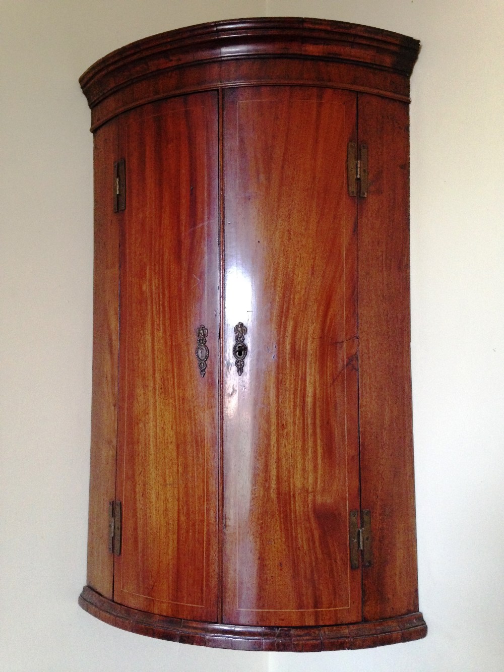 A Sheraton mahogany bow fronted hanging corner cupboard, the cavetto cornice above an interior