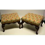 A pair of Edwardian mahogany footstools, with needlework stuffed over seats, the scrolling friezes