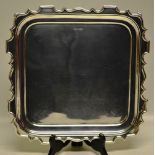 A square salver, with raised piecrust border, on four scroll edge panel feet, 13in (33cm). Makers