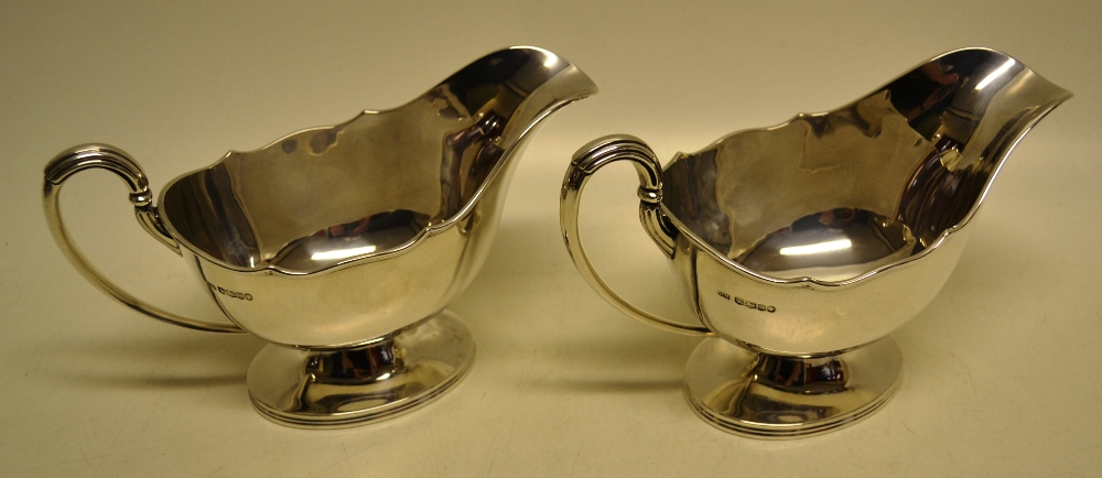 A pair of oval silver sauce boats, having a moulded rim, cast reeded capped lined scroll handles