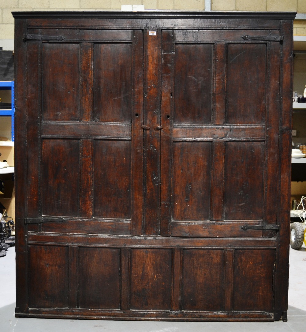 A seventeenth century oak panelled wardrobe, the pair of doors with wrought iron strap hinges. 5ft