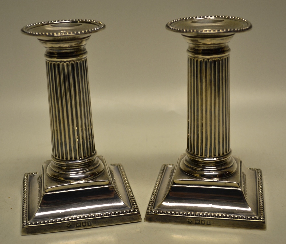 A pair of Edwardian silver reeded pillar boudoir candlesticks, with beaded edge nozzles and flared