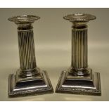 A pair of Edwardian silver reeded pillar boudoir candlesticks, with beaded edge nozzles and flared