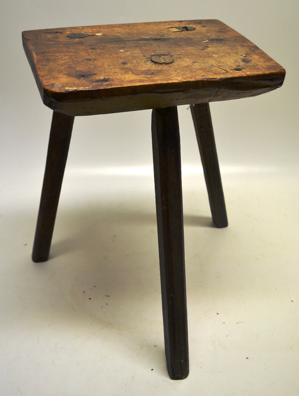 An early nineteenth century country made milking stool, the tapering walnut seat on three facetted