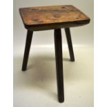An early nineteenth century country made milking stool, the tapering walnut seat on three facetted