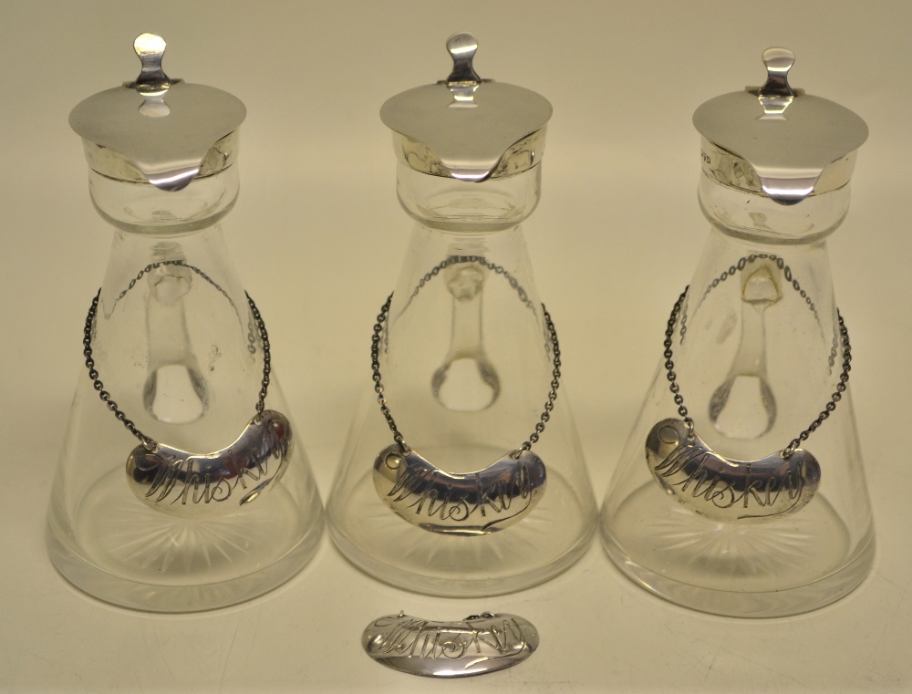 A set of three George V glass whisky tots with hinged silver covers, together with a set of four