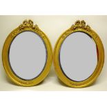 A pair of Victorian oval mirrors, the gilt frames with ribbon tied foliage surmounts in cast