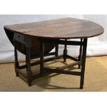 An antique oak gateleg table, the oval drop leaf top above an end frieze drawer, on baluster