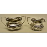 An Edwardian silver sugar and cream set, the partly ribbed ogee rectangular bodies with gadroon