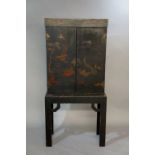 A Chinese black lacquer cabinet on stand enclosed by a pair of doors decorated with fanciful birds