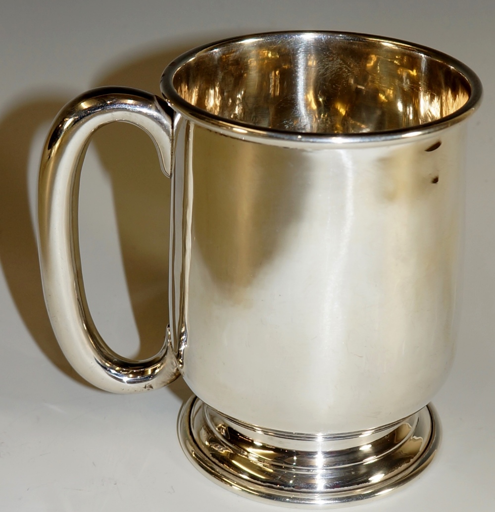 A plain tankard of slightly tapered bellied form on circular stepped foot with plain C-loop handle,