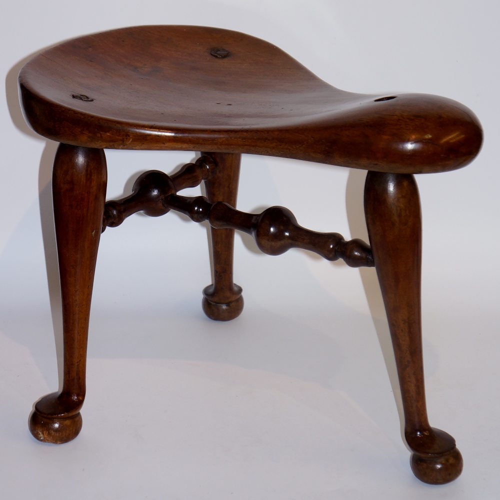 A saddled formed stool on three turned tapered legs with pad feet turned by bold T-shaped stretcher,