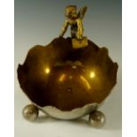 A nickel plated brass bowl as a stylised half egg with winged amorini, three sphere feet, 18cm high,