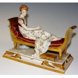A continental porcelain figure of a woman reclining on a regency scroll arm gilt sofa,