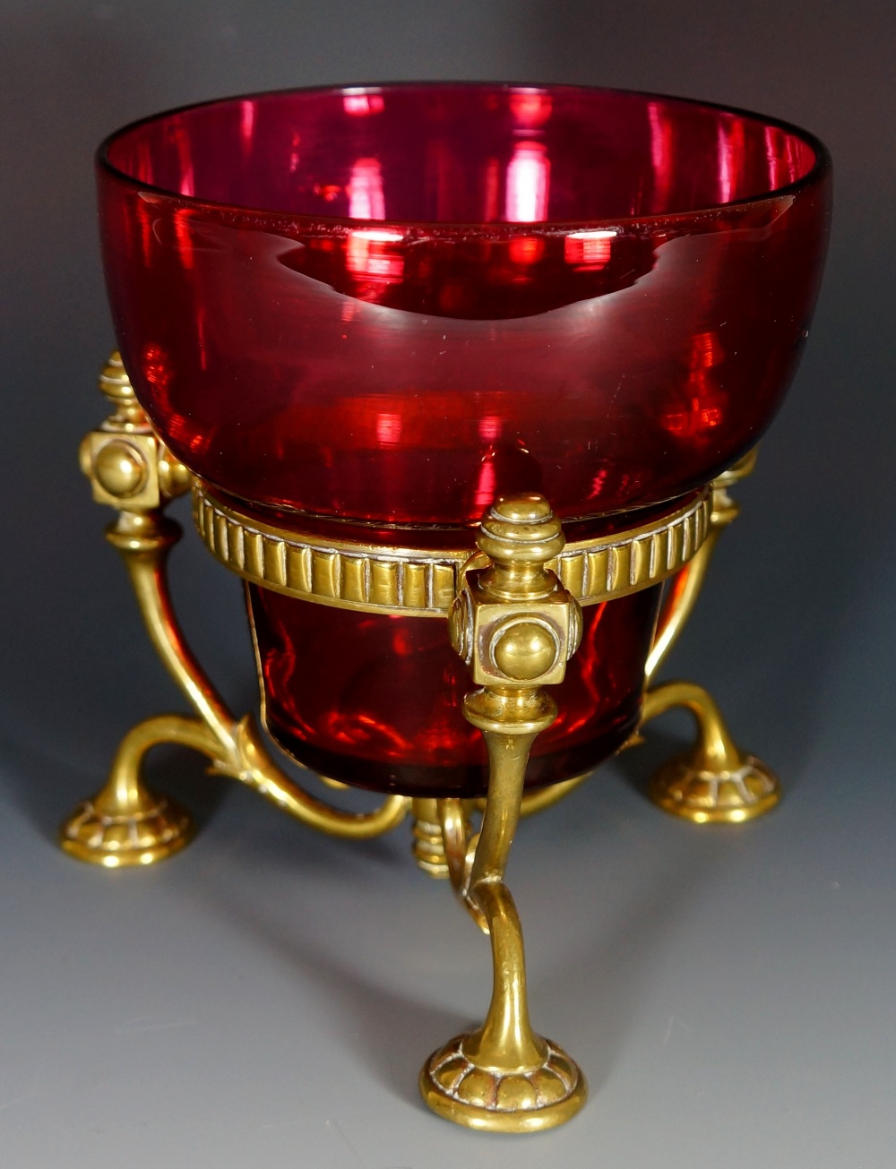 A cranberry glass bowl with tri-footed foliate clasped brass stand,