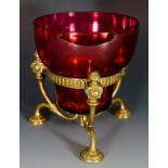 A cranberry glass bowl with tri-footed foliate clasped brass stand,