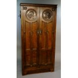 A good Arts and Crafts oak cupboard enclosed by a pair of doors with classical copper roundel heads,