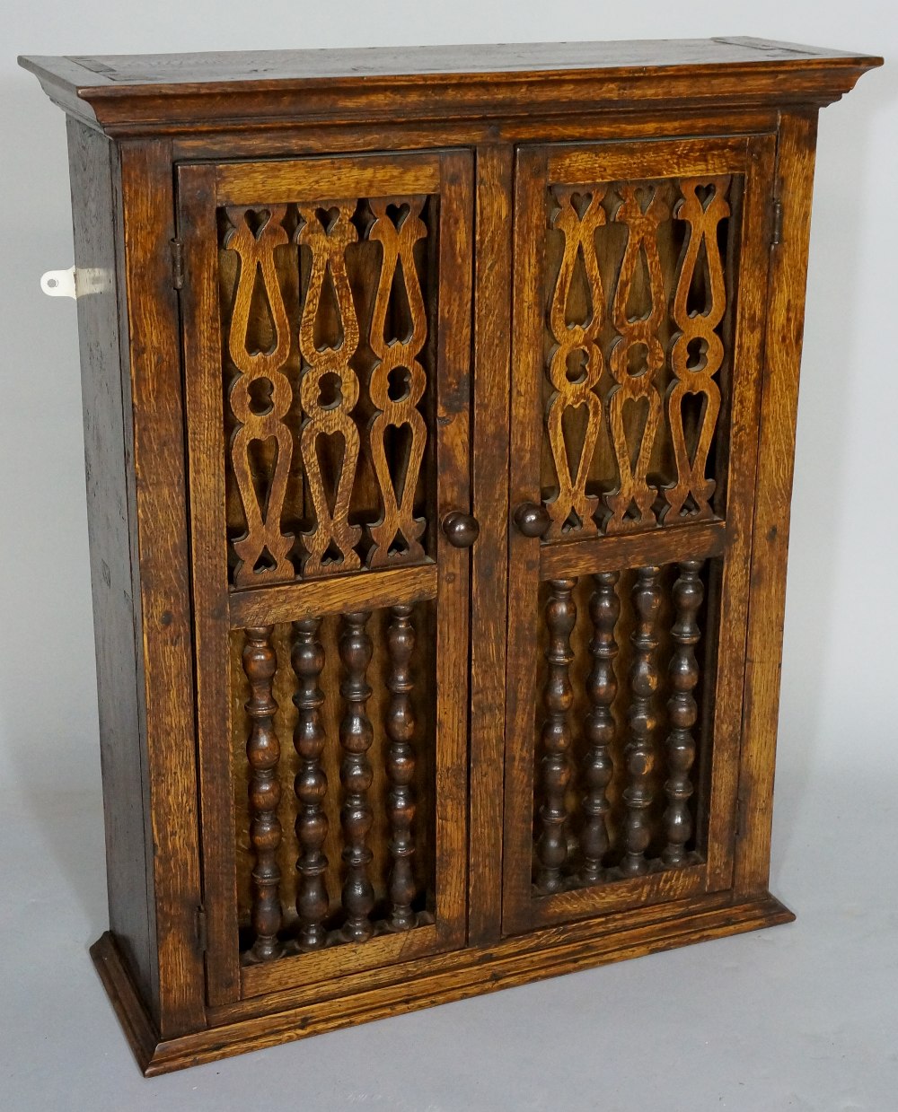 An oak spice cupboard in late 17th Century style the flared cornice above a pair of doors each with