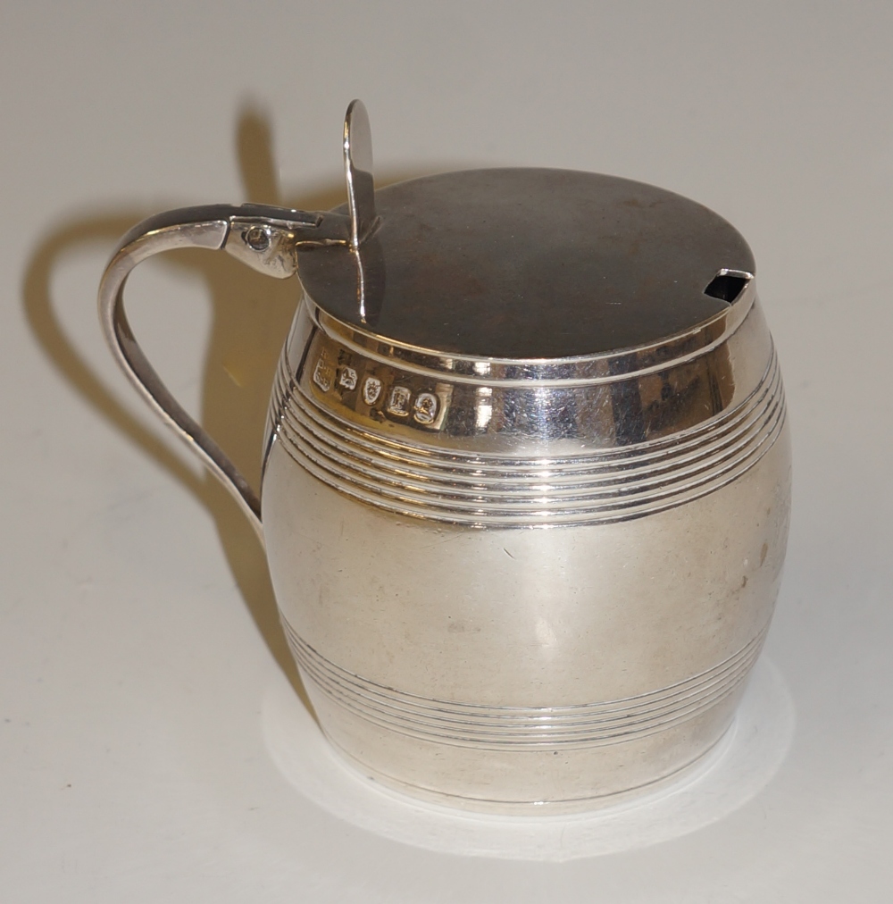 A George III barrel shaped lidded mustard with reeded bands engraved with a crest, scroll handle,