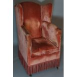 A wing back armchair upholstered in pink velvet on square tapered legs fitted castors, 118cm high,