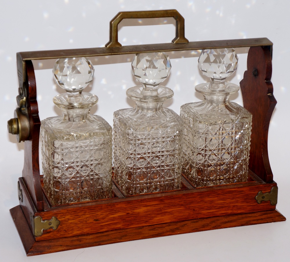 An oak three bottle tantalus with silver plated mounts, each decanter hobnail cut, 34cm wide,