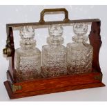 An oak three bottle tantalus with silver plated mounts, each decanter hobnail cut, 34cm wide,