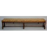 An oak long stool in 17th Century style the upholstered top above turned legs,