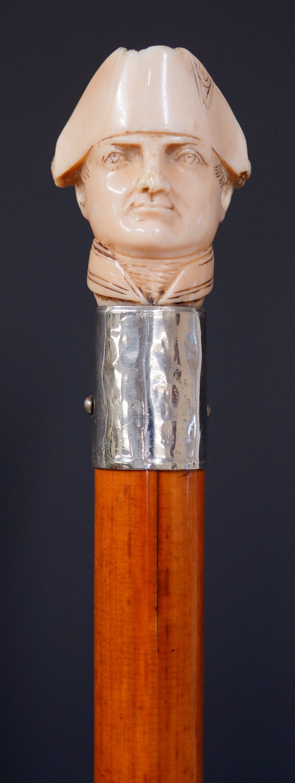 A walking stick the ivory terminal carved with head of Napoleon, silver coloured metal collar,