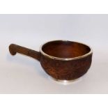 A wooden long handled bowl the body carved with circles and formal leafage underneath a foliate