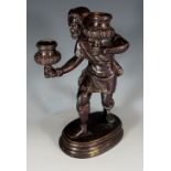A bronze candlestick modelled as a bearded gentleman holding  two foliate cast nozzles, oval base,