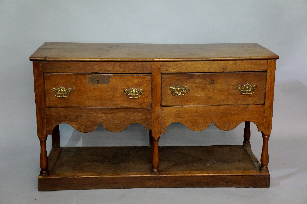 An oak dresser base the rectangular top above a frieze fitted two drawers, shaped apron,