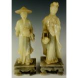 Two soapstone figures of a woman holding basket of fish and a gentleman with basket, square plinths,