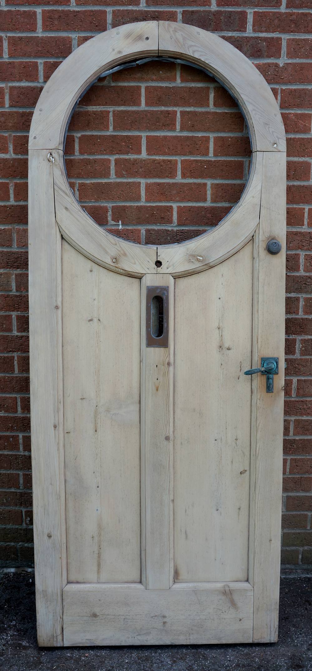 An Edwardian arched pine front door with circular aperture for leaded glass, letter box,
